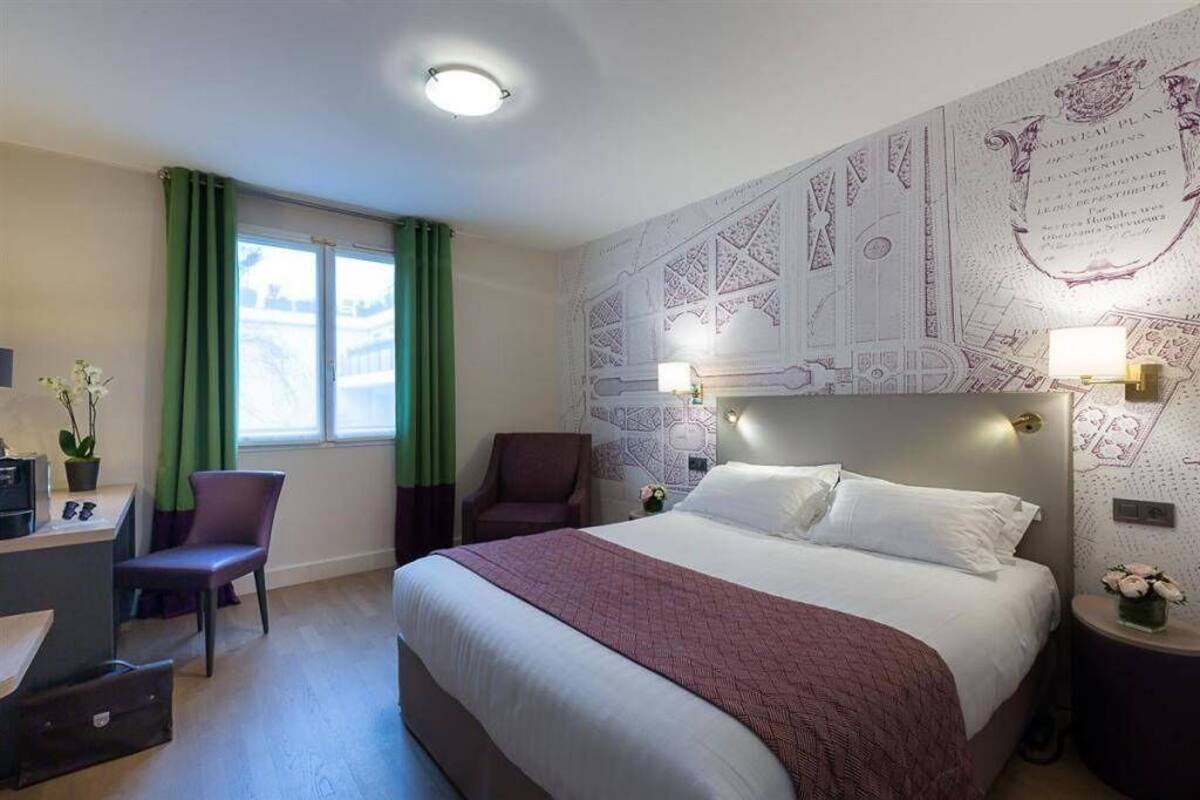 A hotel room with a bed, a desk, a chair, a window with curtains, and a wall with decorative patterns.