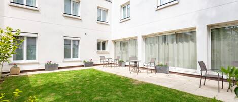 A courtyard with a neatly trimmed lawn, outdoor seating area, and large windows.