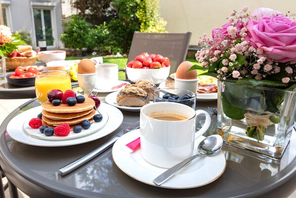 Una mesa de desayuno con panqueques, frutos rojos, café y un ramo de flores.