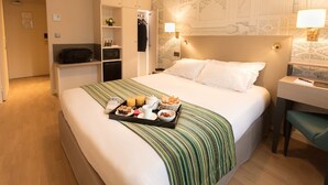 A hotel room with a neatly made bed, a desk, and a tray of breakfast items. - Hôtel Montbriand Antony (Antony)