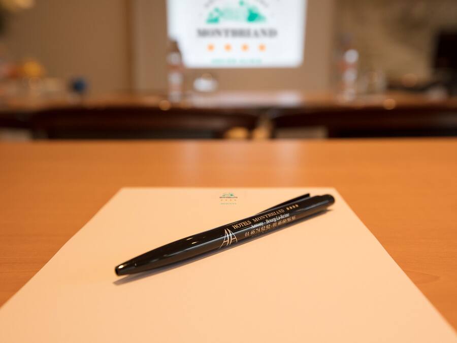 Een zwarte pen op wit papier met hotel branding, een houten tafel en een vage achtergrond met een presentatiescherm.