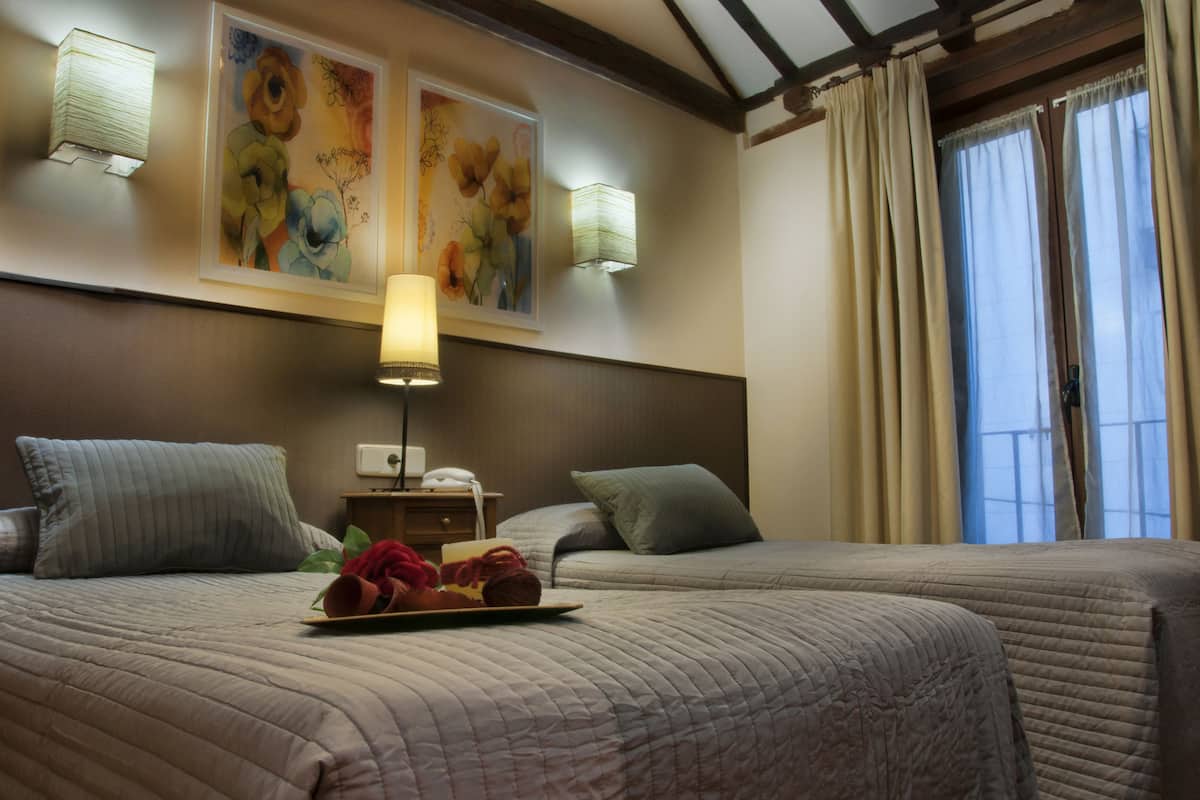 A hotel room with two beds, a nightstand with a lamp, and artwork on the wall.