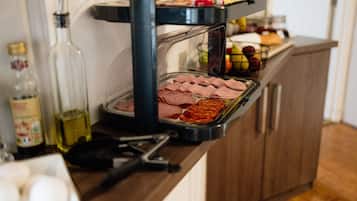 A kitchen counter with a sandwich press containing sliced meats and a fruit basket.