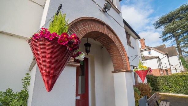 A building with a red door, a brick archway, and hanging flower baskets. - Red Mullions Guest House (Oxford)