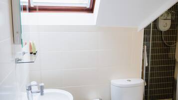 A modern bathroom with a skylight, white tiles, a sink, a toilet, and a shower area.