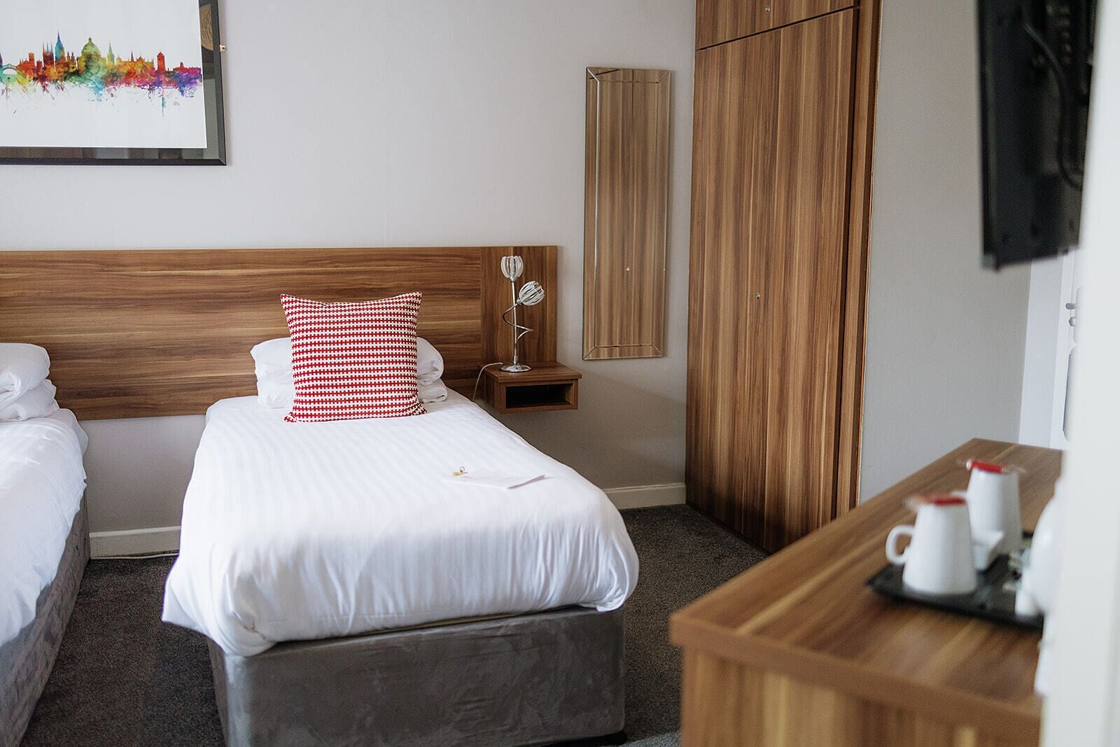 Ein Hotelzimmer mit zwei Betten, einem Holzschrank, einem Nachttisch mit Lampe und einem kleinen Tisch mit Tassen.