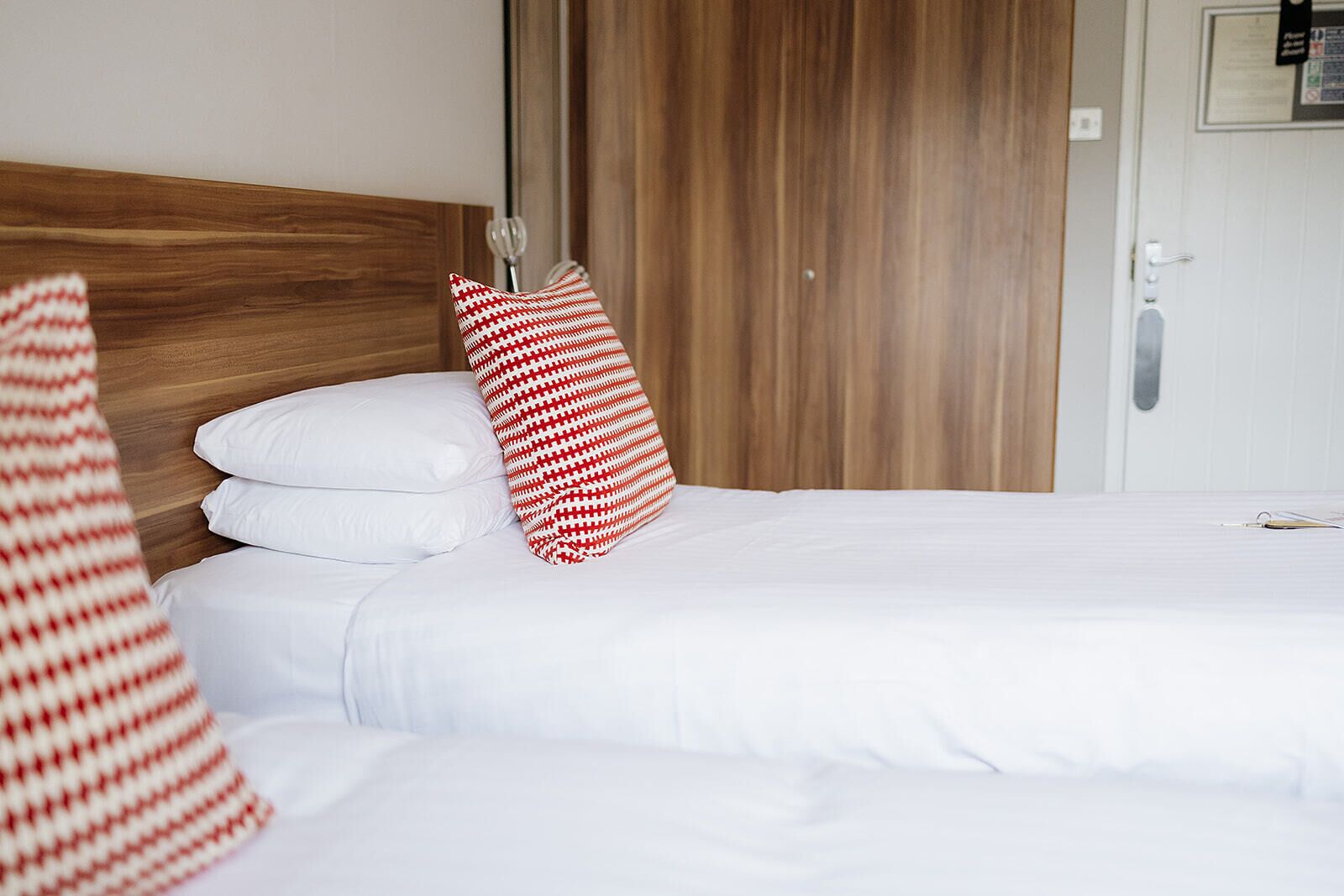 A hotel room with a wooden headboard, white bedding, and a red and white striped pillow.