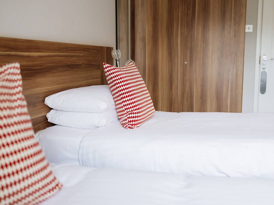 A hotel room with a wooden headboard, white bedding, and a red and white striped pillow.