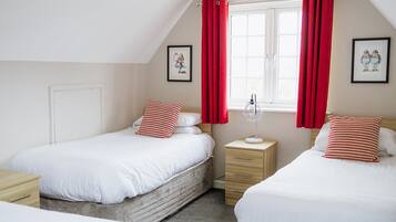 A bedroom with two single beds, a nightstand with a lamp, and a window with red curtains.