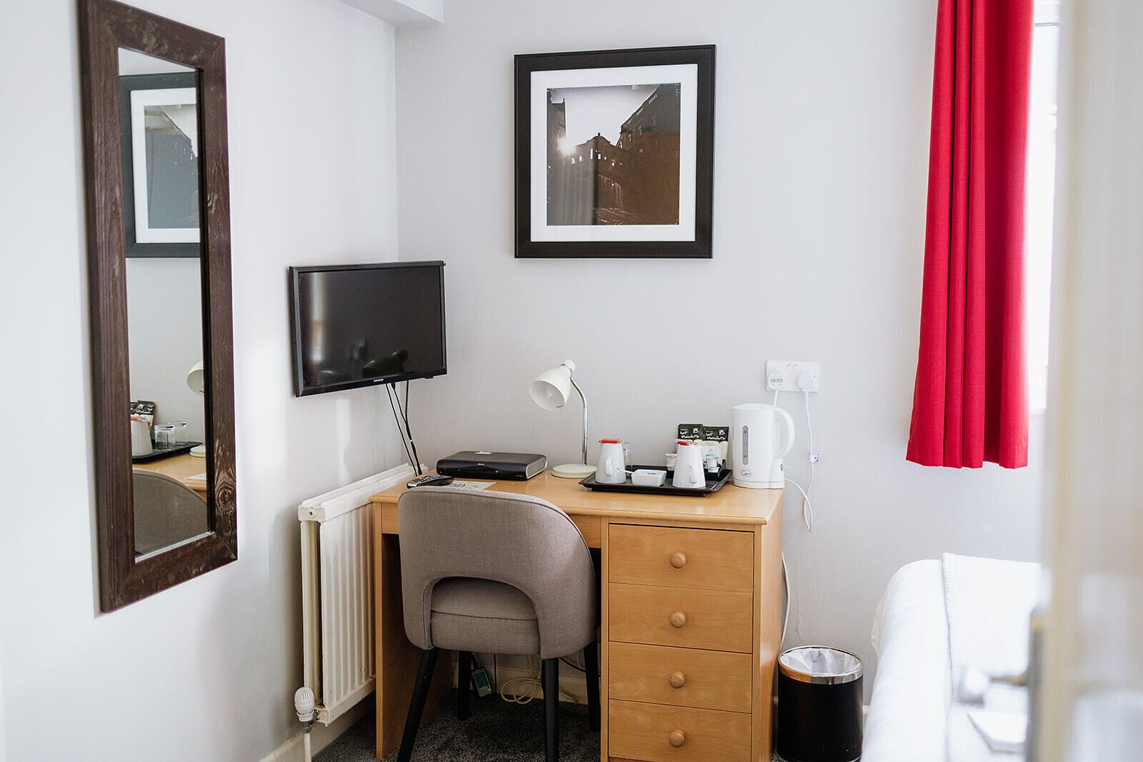 A hotel room with a desk, chair, TV, and a framed picture on the wall.