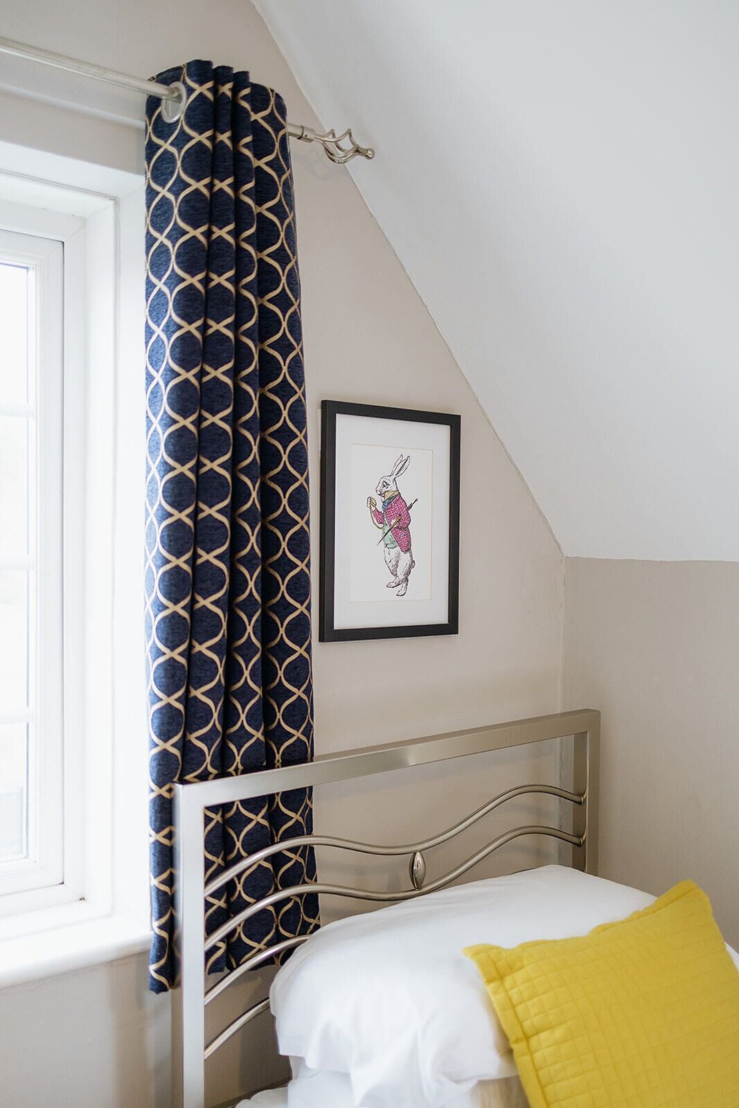 Une chambre à coucher avec un lit, une fenêtre, un rideau et un tableau encadré accroché au mur.