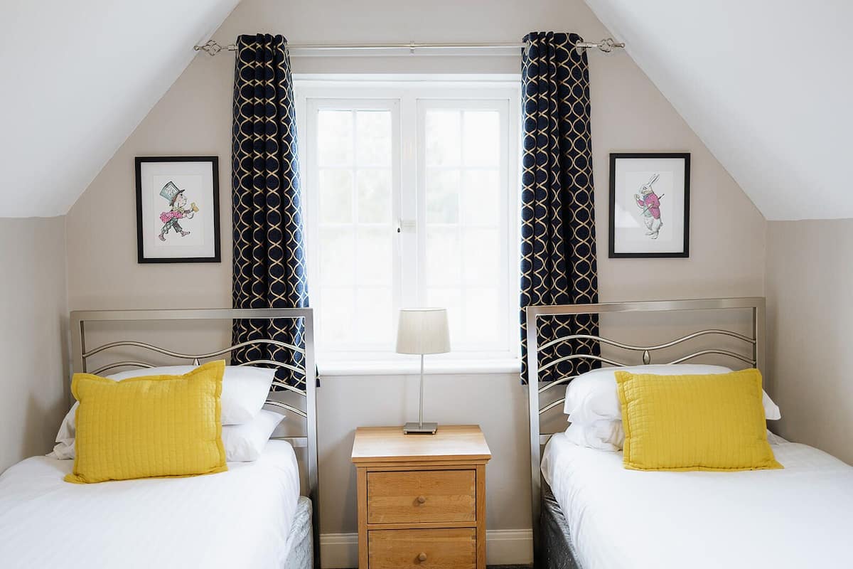 A bedroom with two beds, a nightstand, a window, and two framed pictures on the wall.