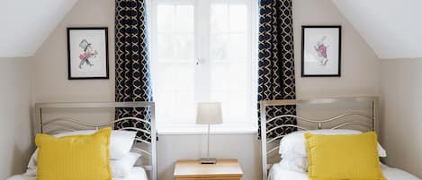 A bedroom with two beds, a nightstand, a window, and two framed pictures on the wall.