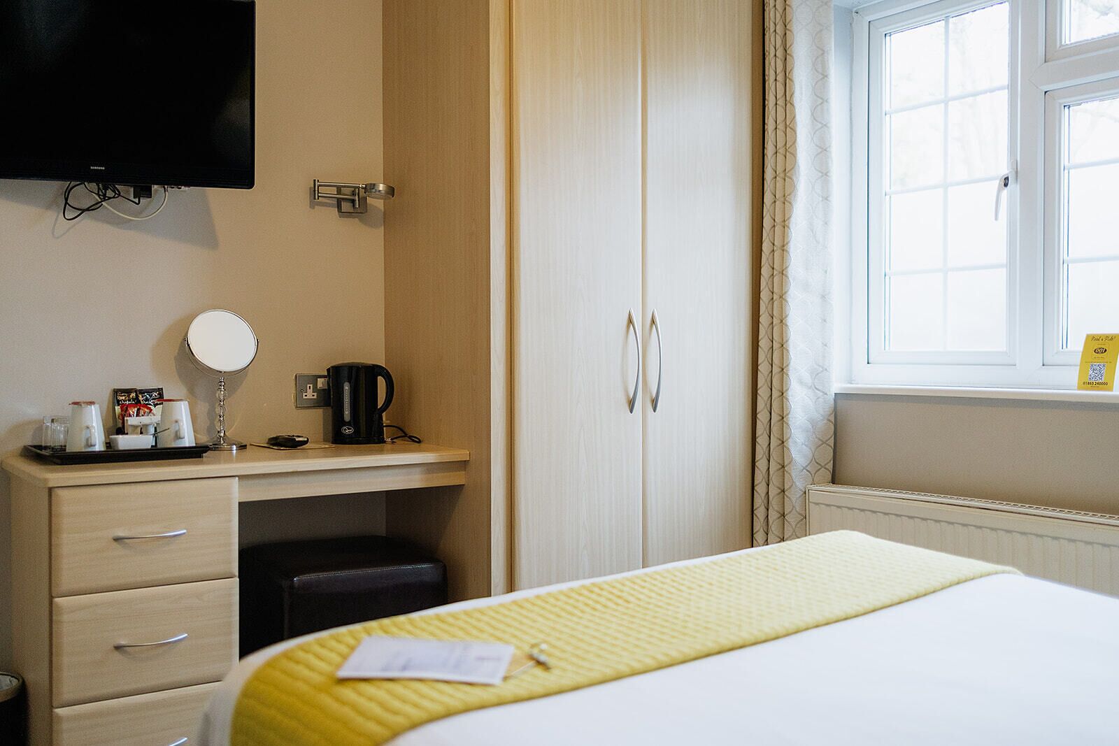 Habitación de hotel con cama, escritorio con espejo, cafetera y televisión montada en la pared.