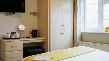 Habitación de hotel con cama, escritorio con espejo, cafetera y televisión montada en la pared.
