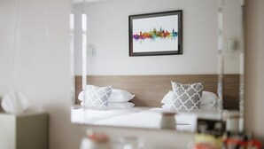 A hotel room with a bed, pillows, a bedside table, and a framed city skyline artwork on the wall. - Red Mullions Guest House (Oxford)