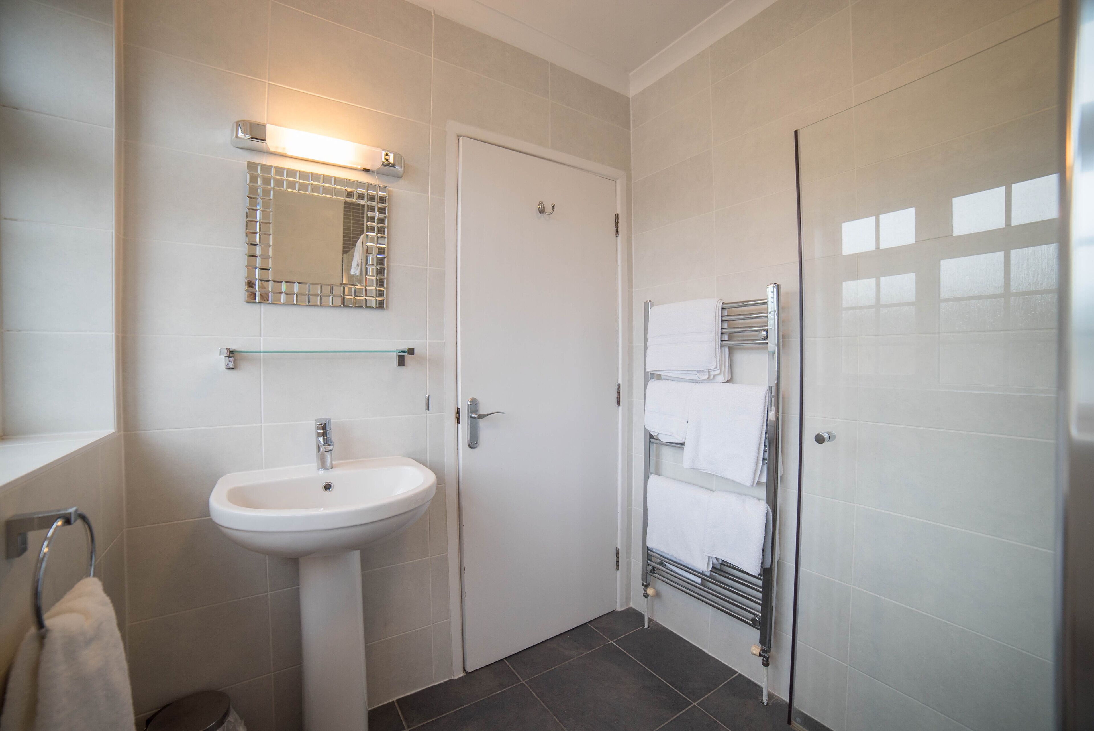 A modern bathroom with a white sink, a mirror with a decorative frame, and a towel rack with multiple towels.