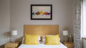 A hotel room with a bed, two bedside lamps, a framed cityscape artwork, and zebra-patterned curtains.