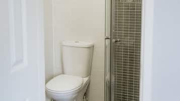 A bathroom with a toilet, a glass shower enclosure, and a towel rack with folded towels.