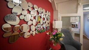 A room with a red wall adorned with various mirrors, a grey armchair, and a small table with a vase of flowers. - Red Mullions Guest House (Oxford)