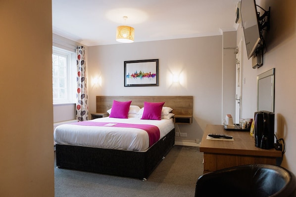 A hotel room with a bed, bedside table, desk, chair, and a large window with curtains.
