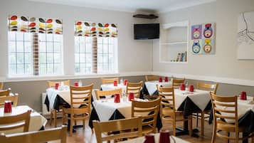 Un espace repas comprenant plusieurs tables et chaises, un téléviseur fixé au mur et une fenêtre donnant sur l’extérieur.