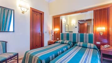 Ein Hotelzimmer mit zwei Betten, einem Holzschrank, Nachttischlampen, einem Sessel und einem Spiegel.