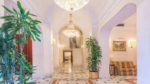 A grand hallway with a large chandelier, marble flooring, and a staircase leading to another area. - Raeli Hotel Lux (Rome)