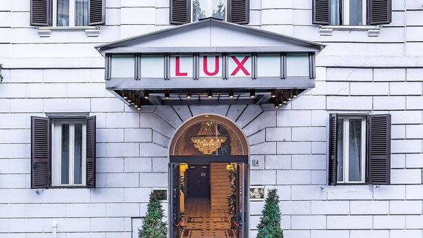 A building facade with a classical architectural style, featuring a central entrance with a decorative archway and the word "LUX" displayed prominently above the entrance. - Raeli Hotel Lux (Rome)