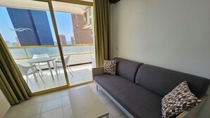 Una sala de estar moderna con un sofá gris, cojines estampados, una mesita blanca y vistas a un balcón con puerta de cristal.