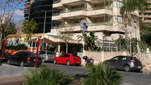 Un hotel de varios pisos con balcones, zona de estacionamiento y vegetación circundante.