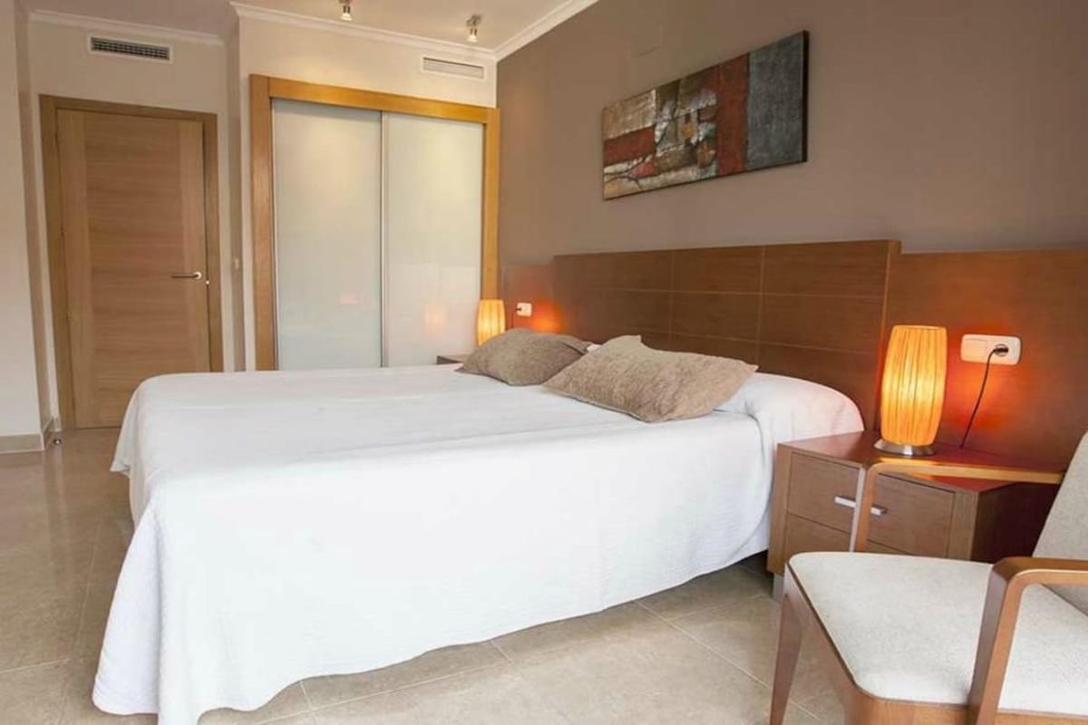 Une chambre d’hôtel avec deux lits, une tête de lit en bois, des lampes de chevet, une chaise et un tableau au mur.