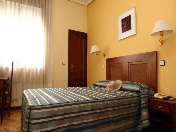 A hotel room with a bed, a nightstand, a chair, a desk, and a window with curtains.