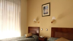Ein Hotelzimmer mit zwei Einzelbetten, einem Holzkopfteil, einem Nachttisch mit Lampe und einem gerahmten Bild an der Wand.