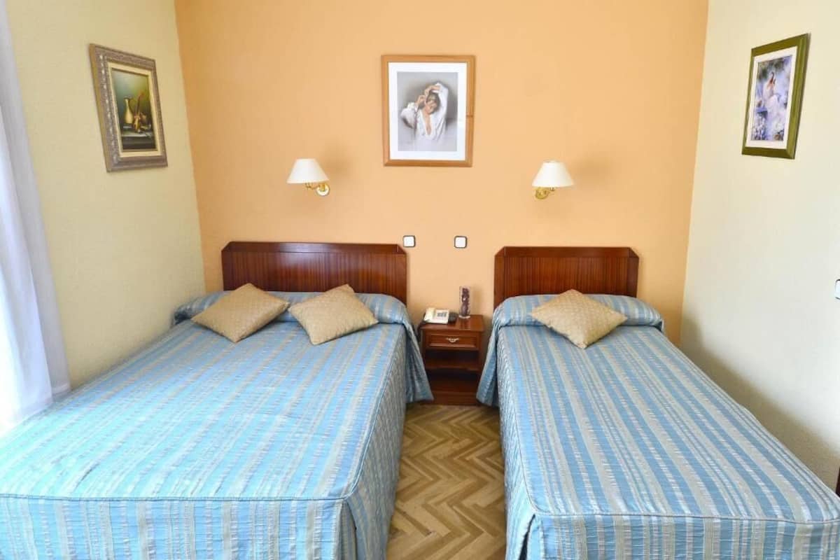 A hotel room with two single beds, a wooden headboard, a nightstand, and a framed picture on the wall.