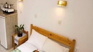 A bedroom with a wooden bed, a bedside table, a small nightstand, and a wall-mounted light fixture. - Anemi Apartments (Hersonissos)