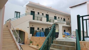 A multi-story building with a staircase leading to the entrance, outdoor seating, and a pool area. - Anemi Apartments (Hersonissos)