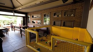 A play area with a yellow padded wall and a fenced playpen containing toys. - Anemi Apartments (Hersonissos)