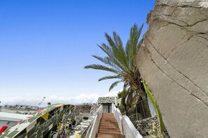 Stunning staircase leads to a building with a mosaic facade, flanked by a palm tree and a rocky cliff.