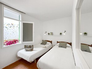Two single beds with white bedding, a large window, and a balcony with a view of a colorful mosaic wall.