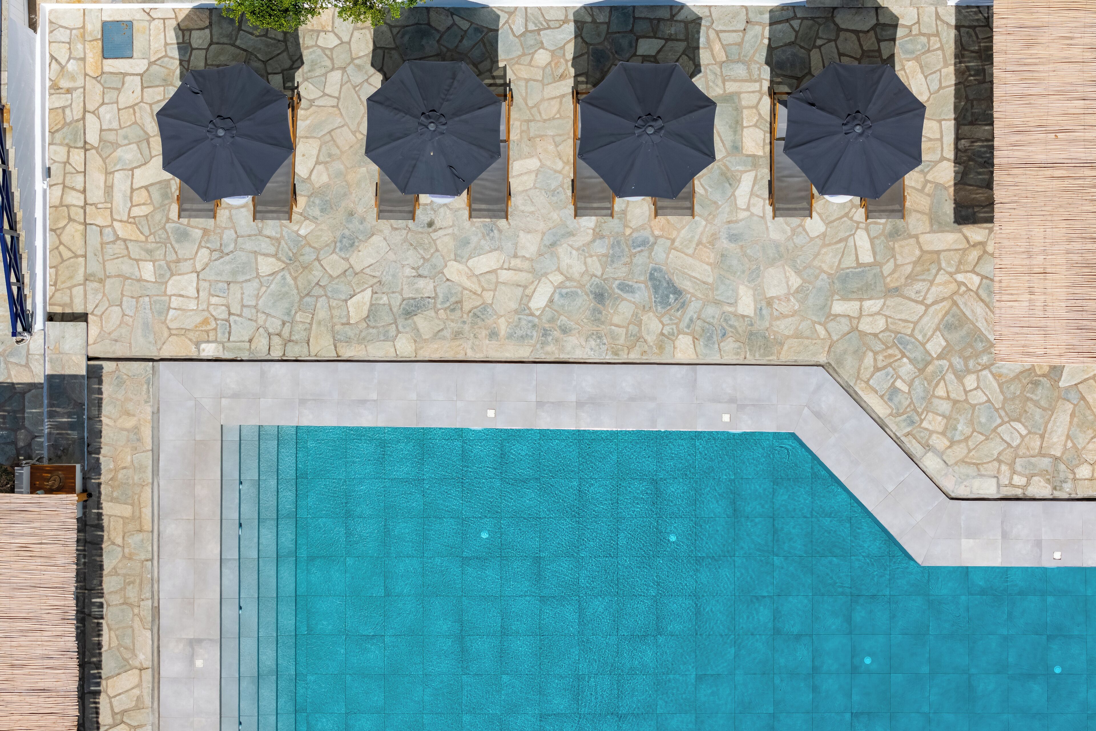 Un espace piscine aménagé sur le toit, avec un sol en pierre et quatre parasols.