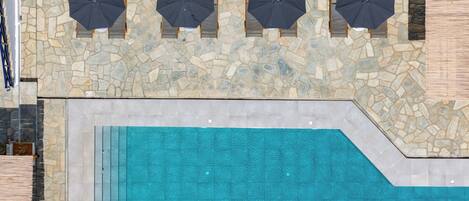 A rooftop pool area with stone flooring and four umbrellas.