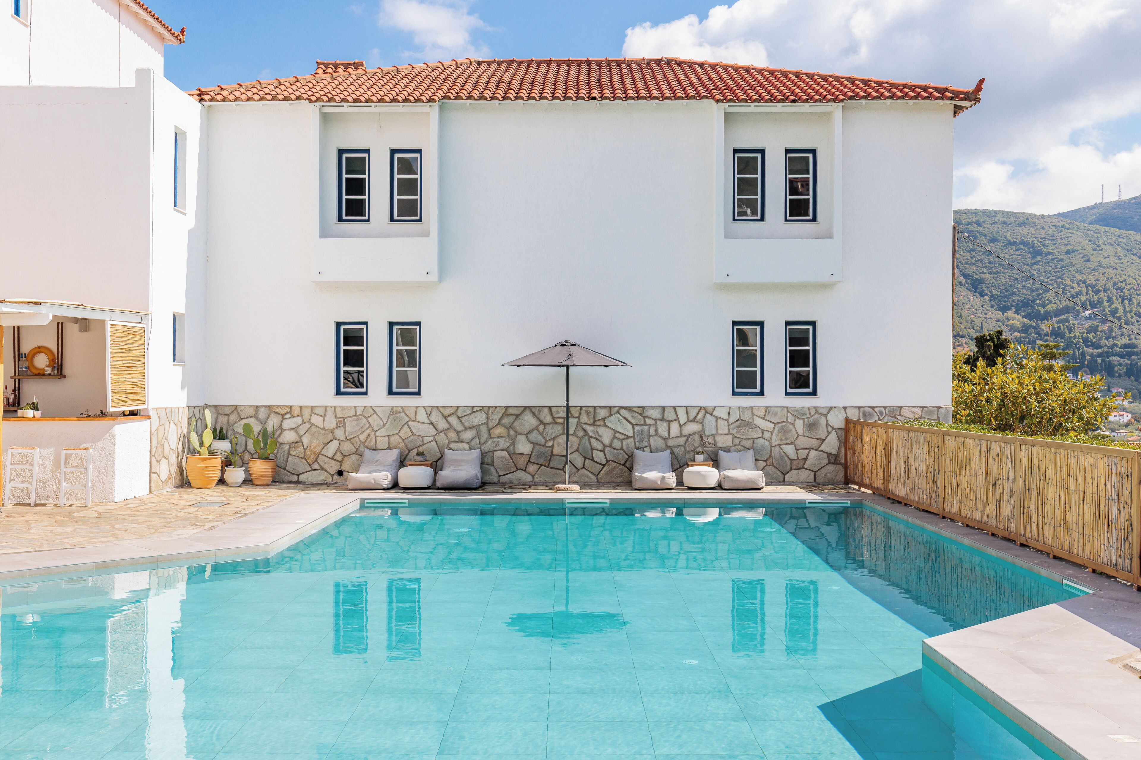 A two-story building with a swimming pool, stone wall, and a view of a mountain.