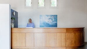 A reception desk with a wooden finish, a large abstract painting, and three small windows above.