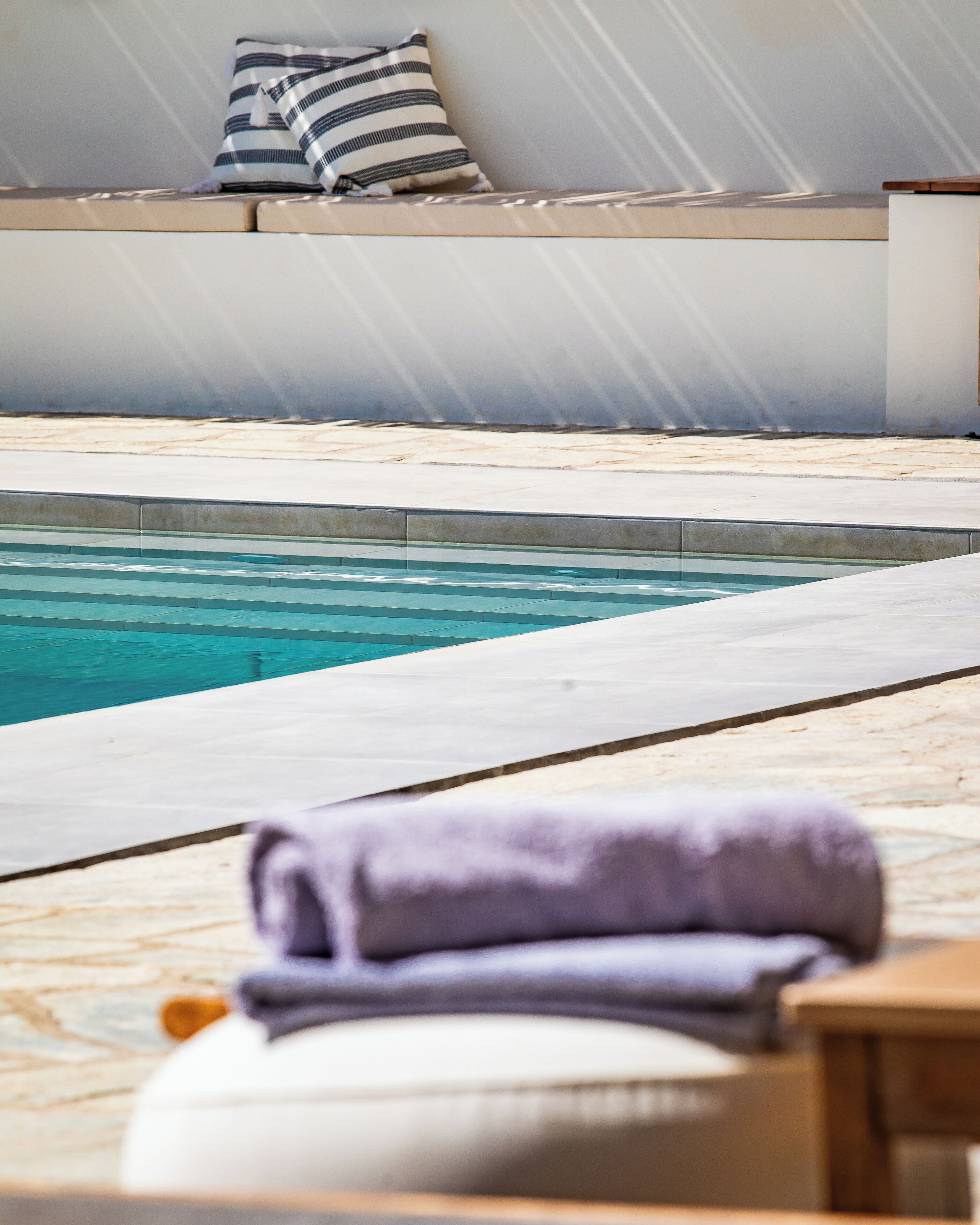 A pool area with a lounge chair and a towel, a striped pillow, and a view of the pool.
