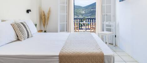 Un dormitorio con cama, televisor, balcón con mesa y silla, y vista a un paisaje montañoso.
