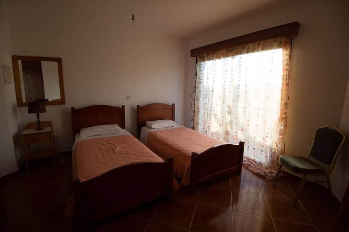 A bedroom with two wooden beds, a nightstand, a chair, a mirror, and a window with curtains.