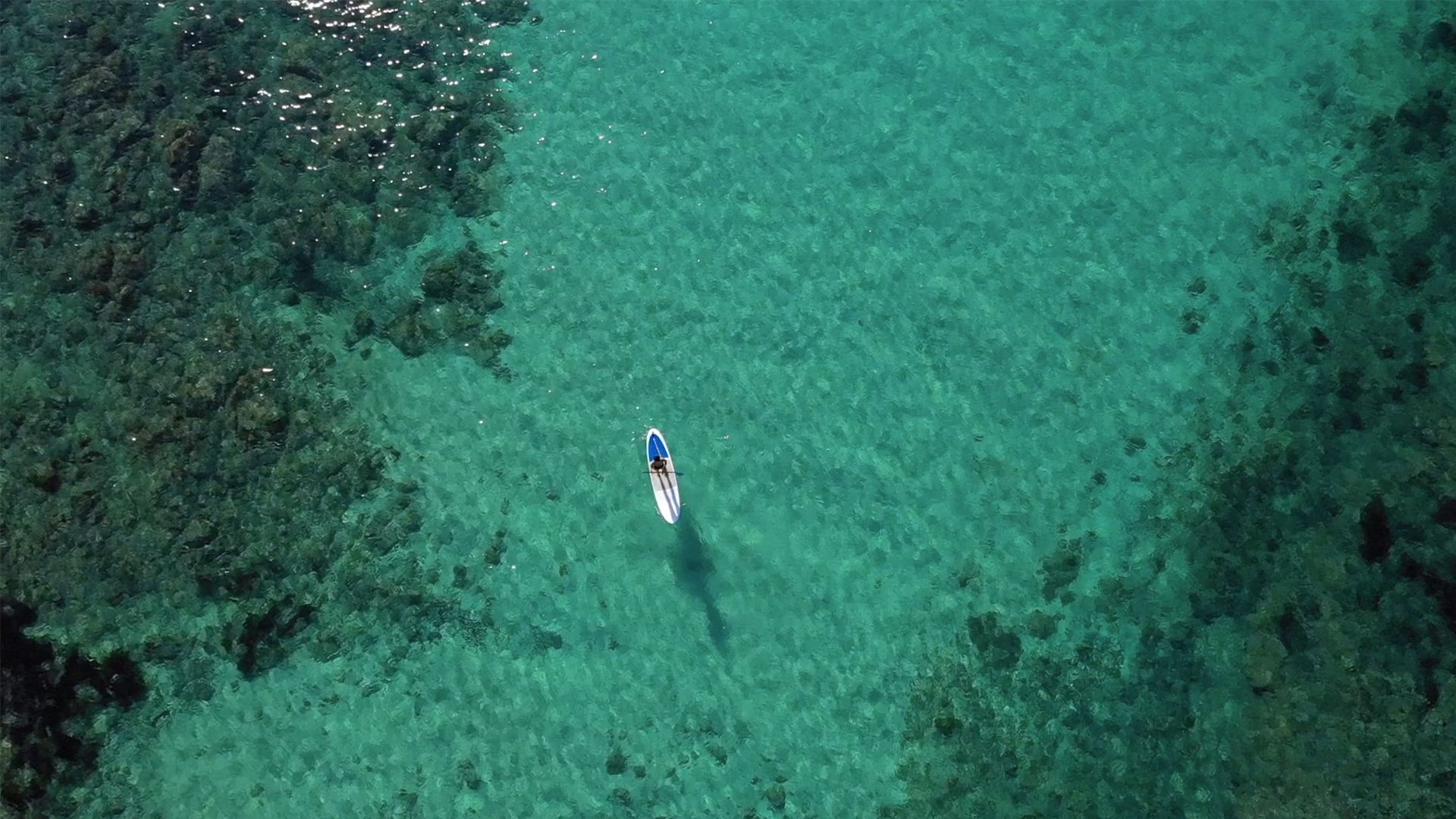 An aerial view of a clear turquoise sea with a single boat in the center.
