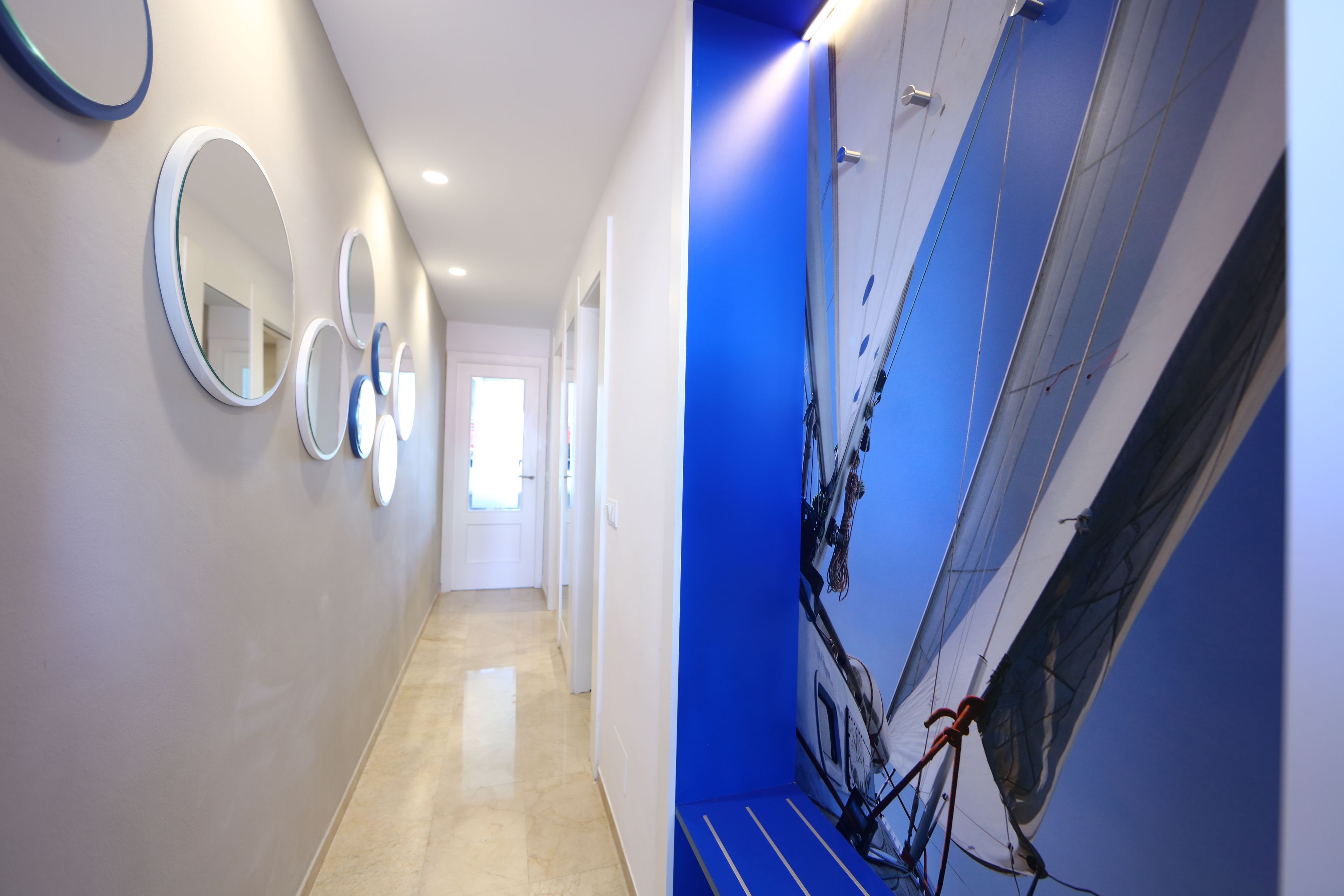 Un pasillo con espejos circulares en la pared, un muro azul decorativo y un mural de un velero.