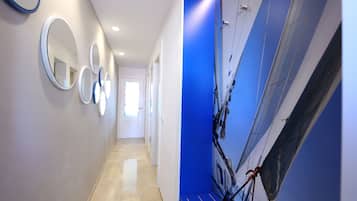 Un pasillo con espejos circulares en la pared, un muro azul decorativo y un mural de un velero.